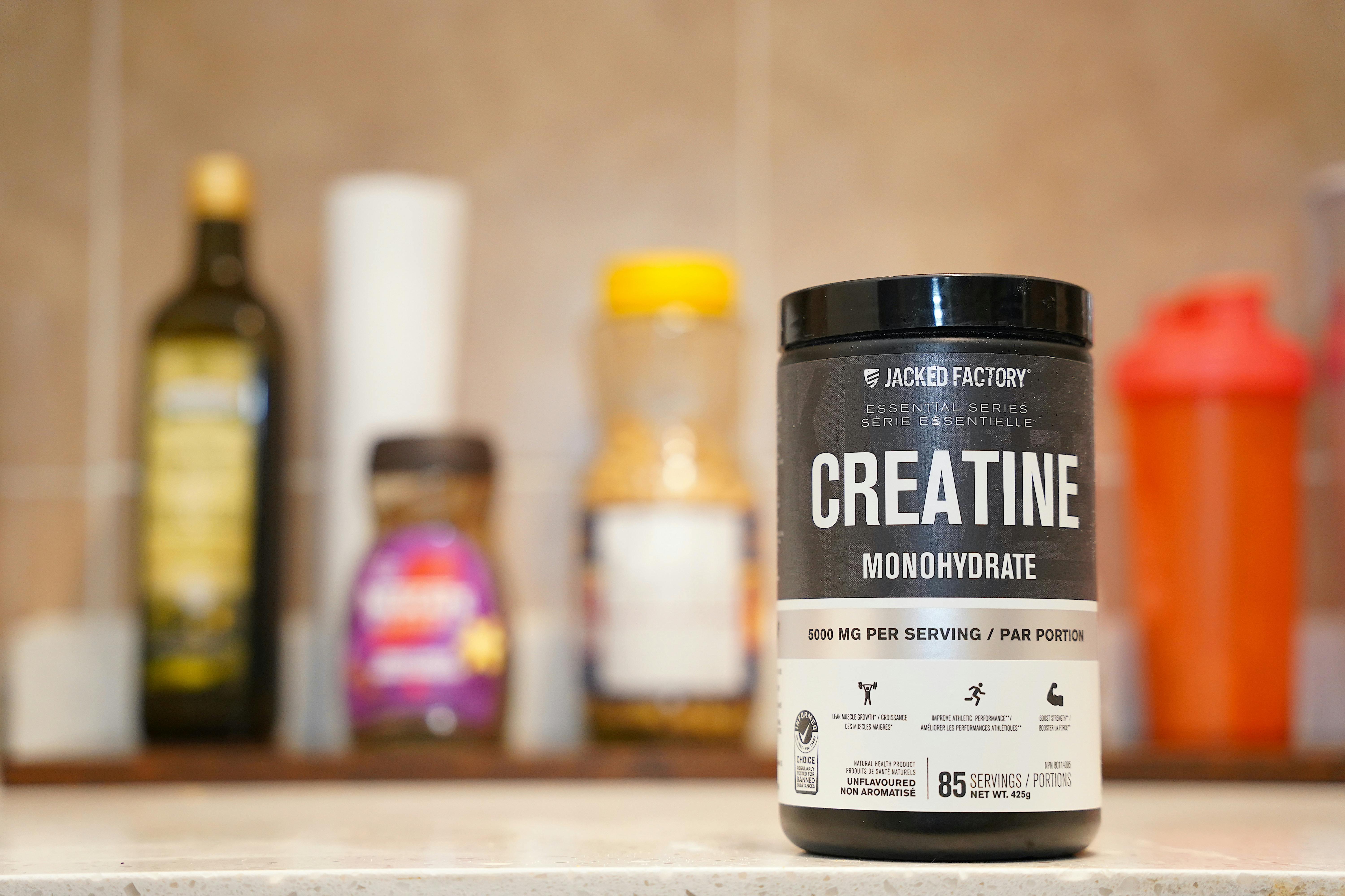 Creatine monohydrate supplement powder in a container on a neutral surface, photographed in natural light
