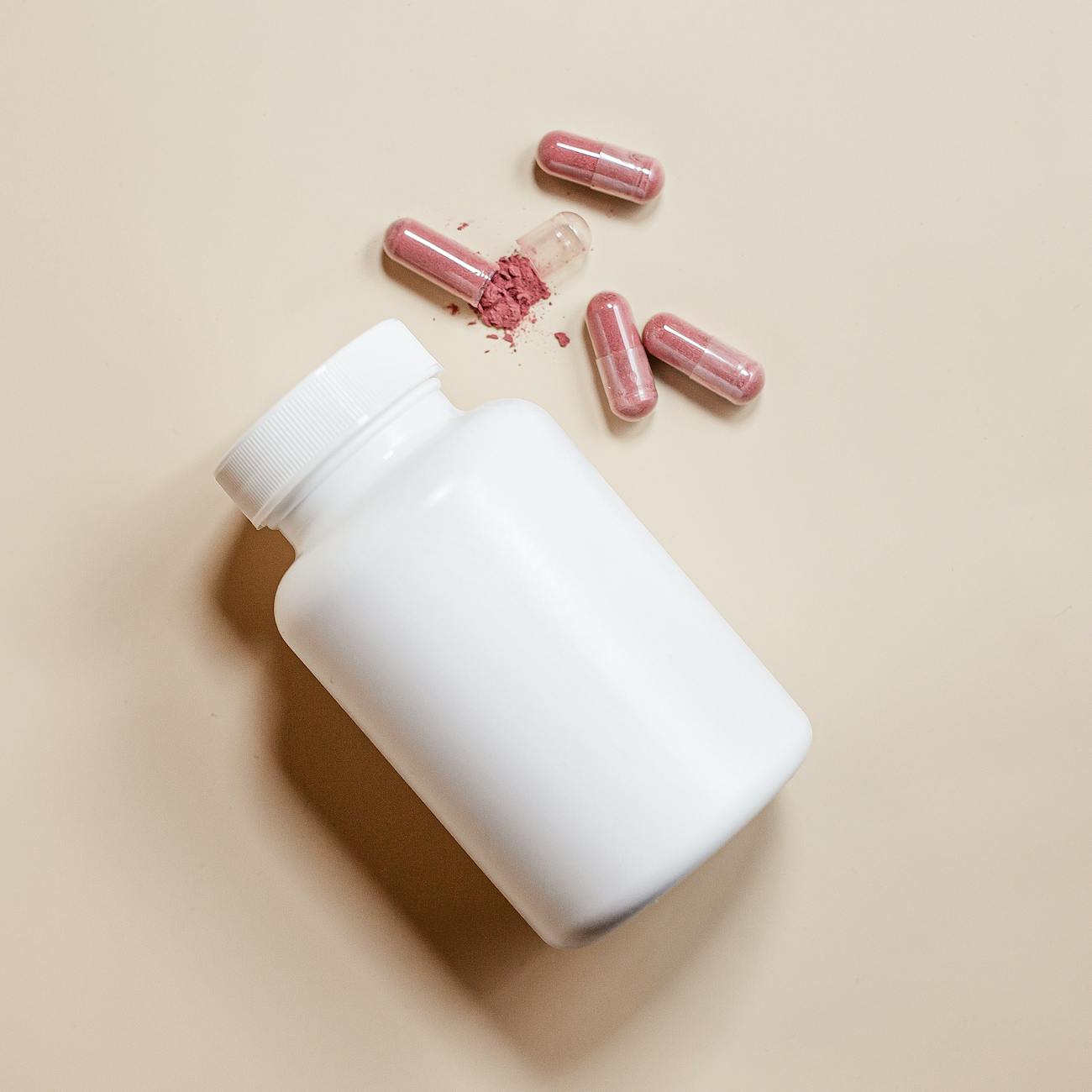 Close-up of a white pill bottle with red capsules on a beige background