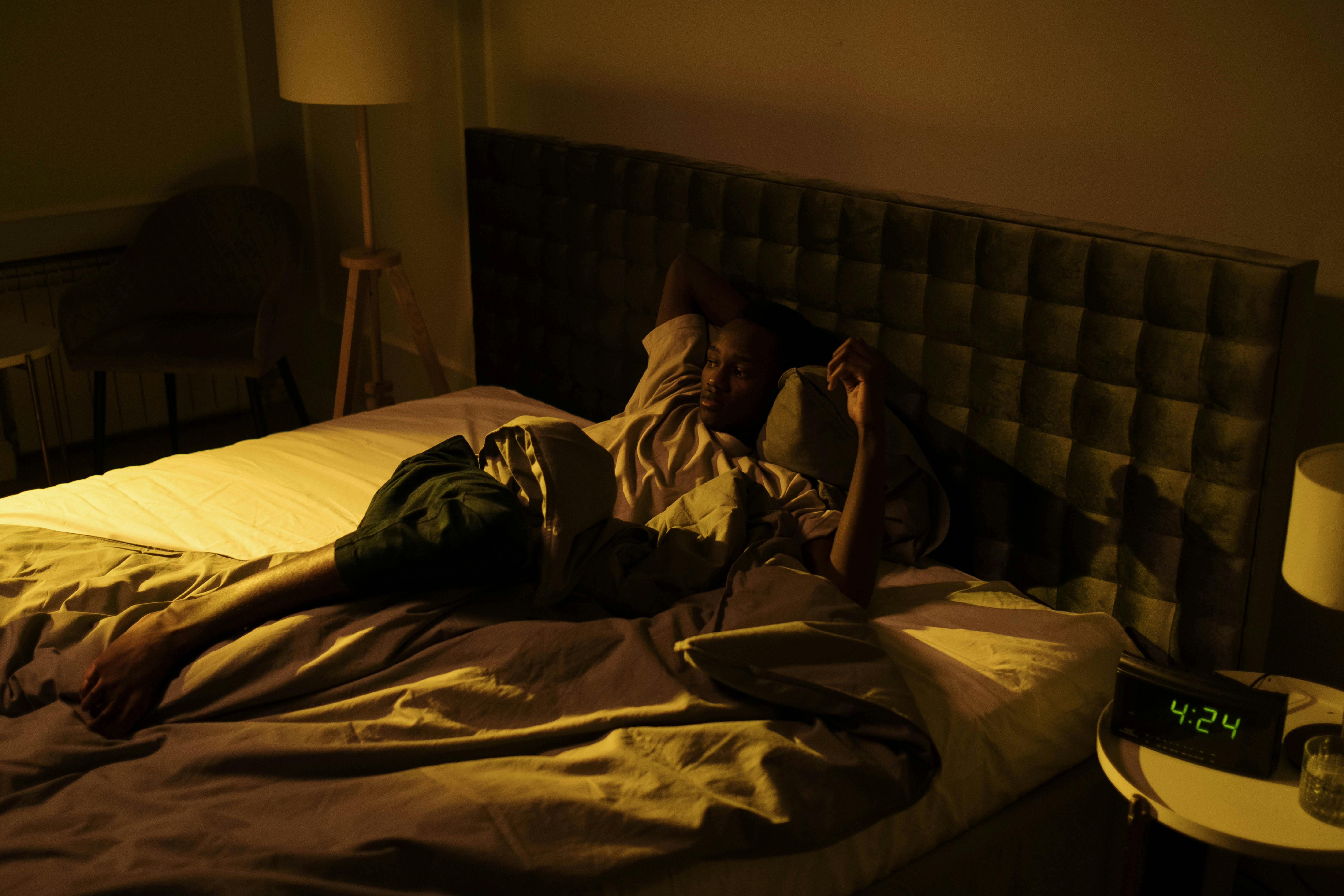 A restless man lying awake on his bed in a dimly lit bedroom at night